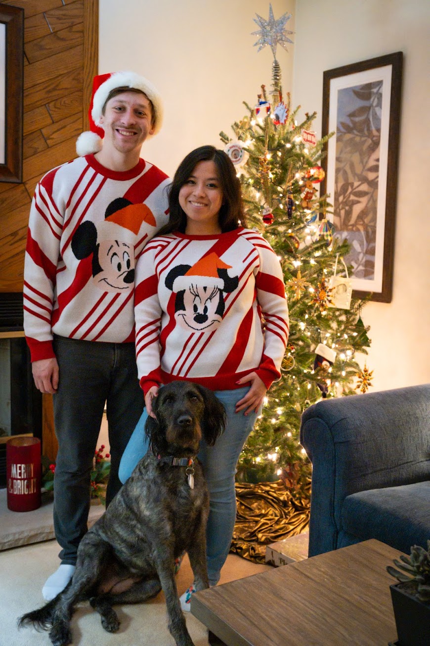 Stephanie, Brandon, and Nyx posing infront of a Christmas tree wearing Christmas sweaters
